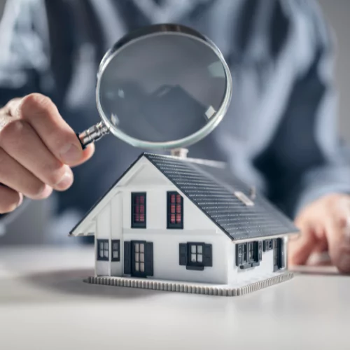 Magnifying glass examining a miniature house, symbolizing real estate data analysis and property research.