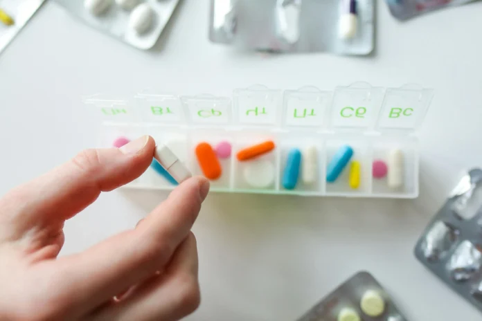 Hand placing a white pill into a weekly pill organizer, symbolizing drug review and transparency connected to the FDA Complete Response Letter database.
