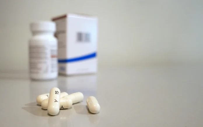 New Mexico prescription drug price comparison illustration showing white capsules in front of medicine bottles and packaging.