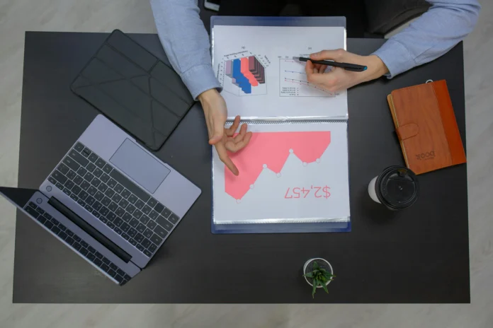 Business analyst reviewing charts and financial reports on a desk with a laptop and documents, representing research in the Vermont Business Entity Search database.