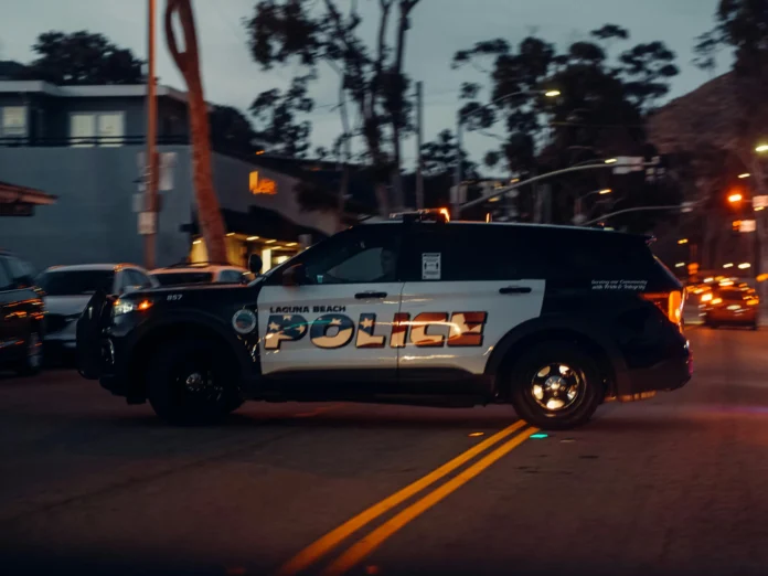 A Laguna Beach police vehicle driving through a California street at dusk, representing law enforcement activity related to the California Law Enforcement Accountability Network Database.